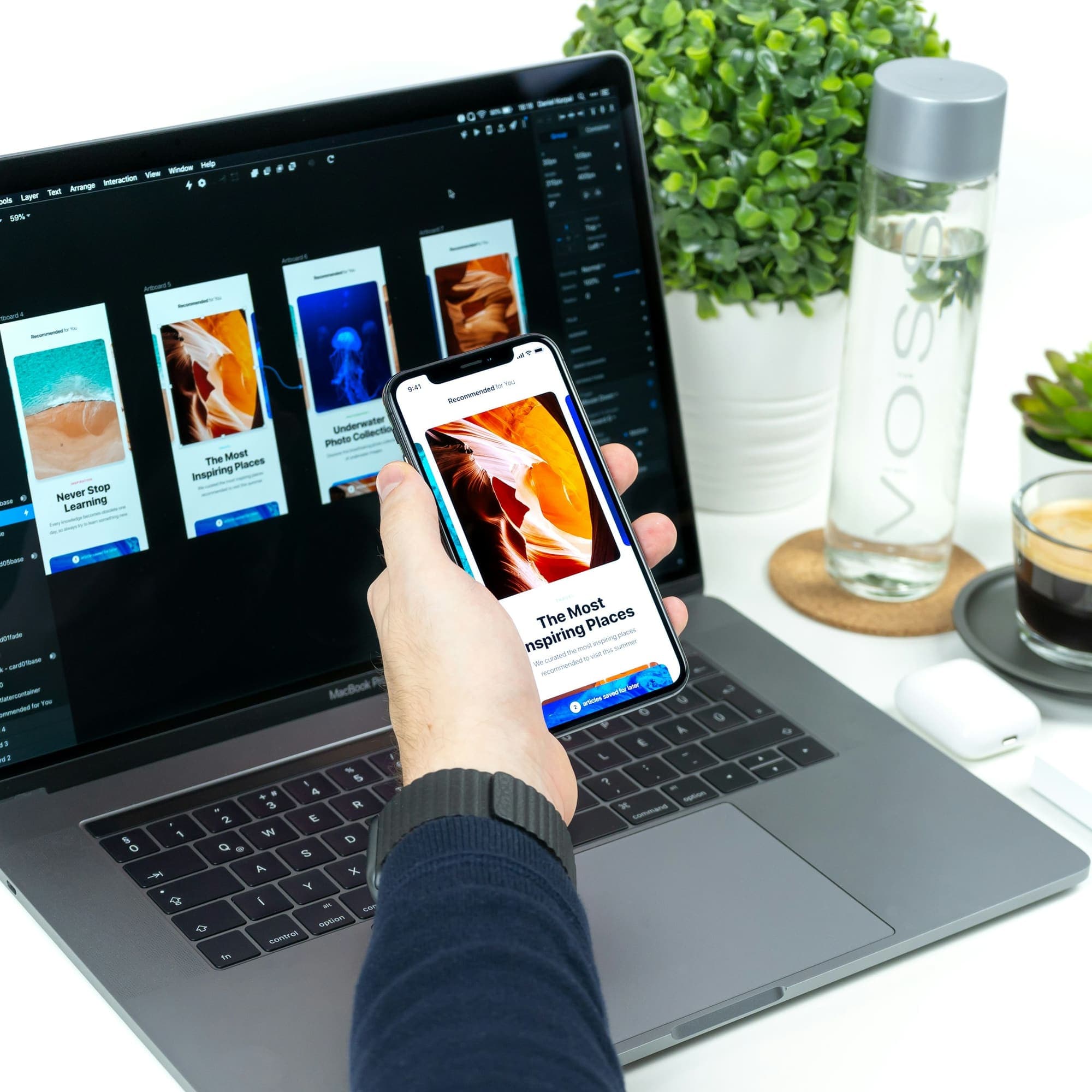 Hand holding a phone showing a mobile site, laptop behind